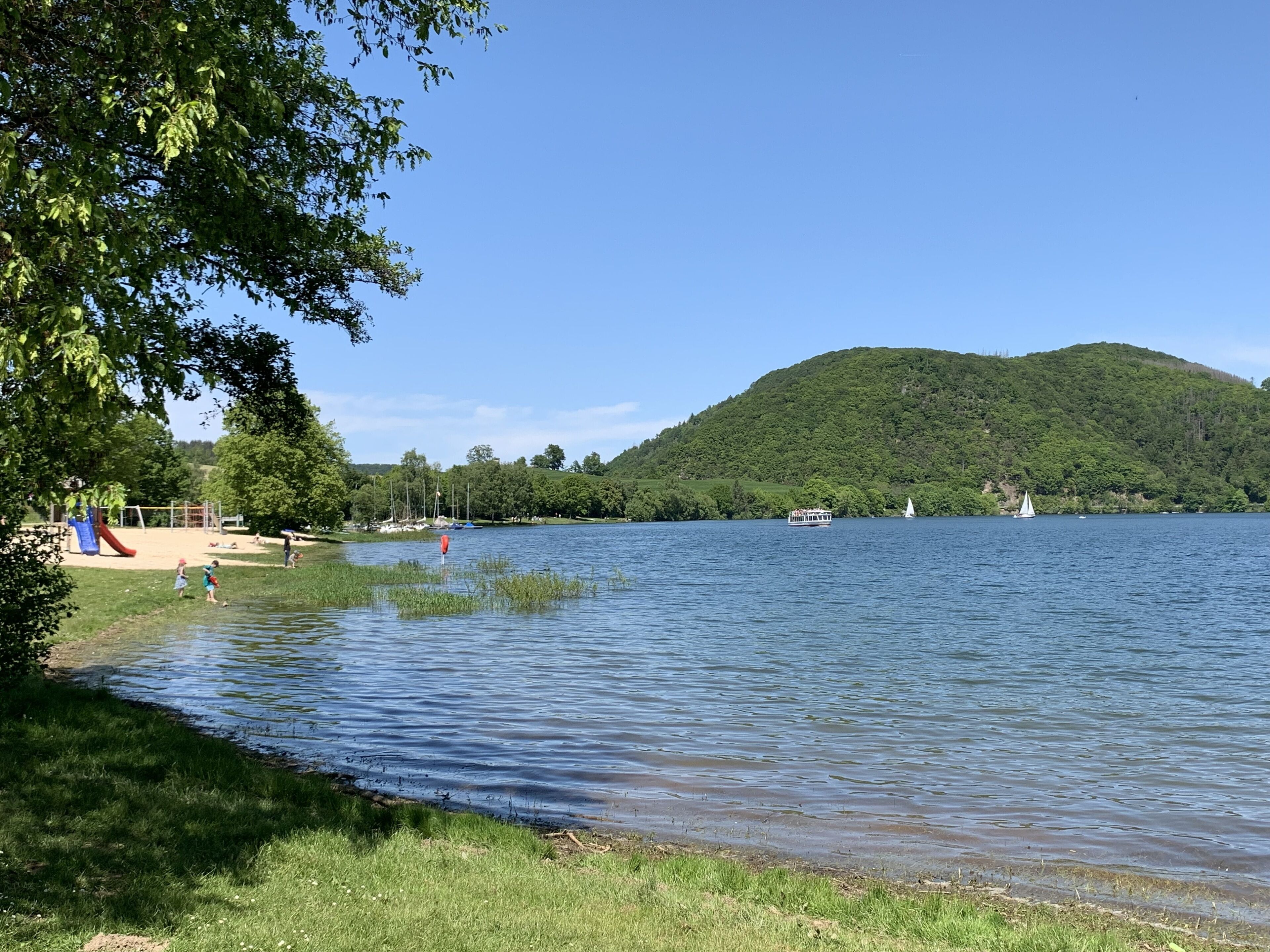 A lakeside view with a grassy area, a playground, and a boat on the water.