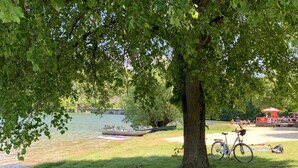 A park with a lake, a tree, a bicycle, and a red structure in the background. - Ferienwohnung Sauerlandblick (Korbach)