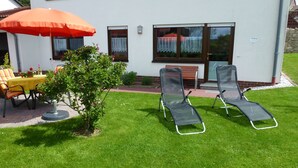 A patio with two lounge chairs, a table with a yellow tablecloth, and an orange umbrella. - Ferienwohnung Sauerlandblick (Korbach)