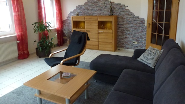 A living room with a sofa, a wooden coffee table, a chair, a stone wall, and a wooden cabinet. - Ferienwohnung Sauerlandblick (Korbach)