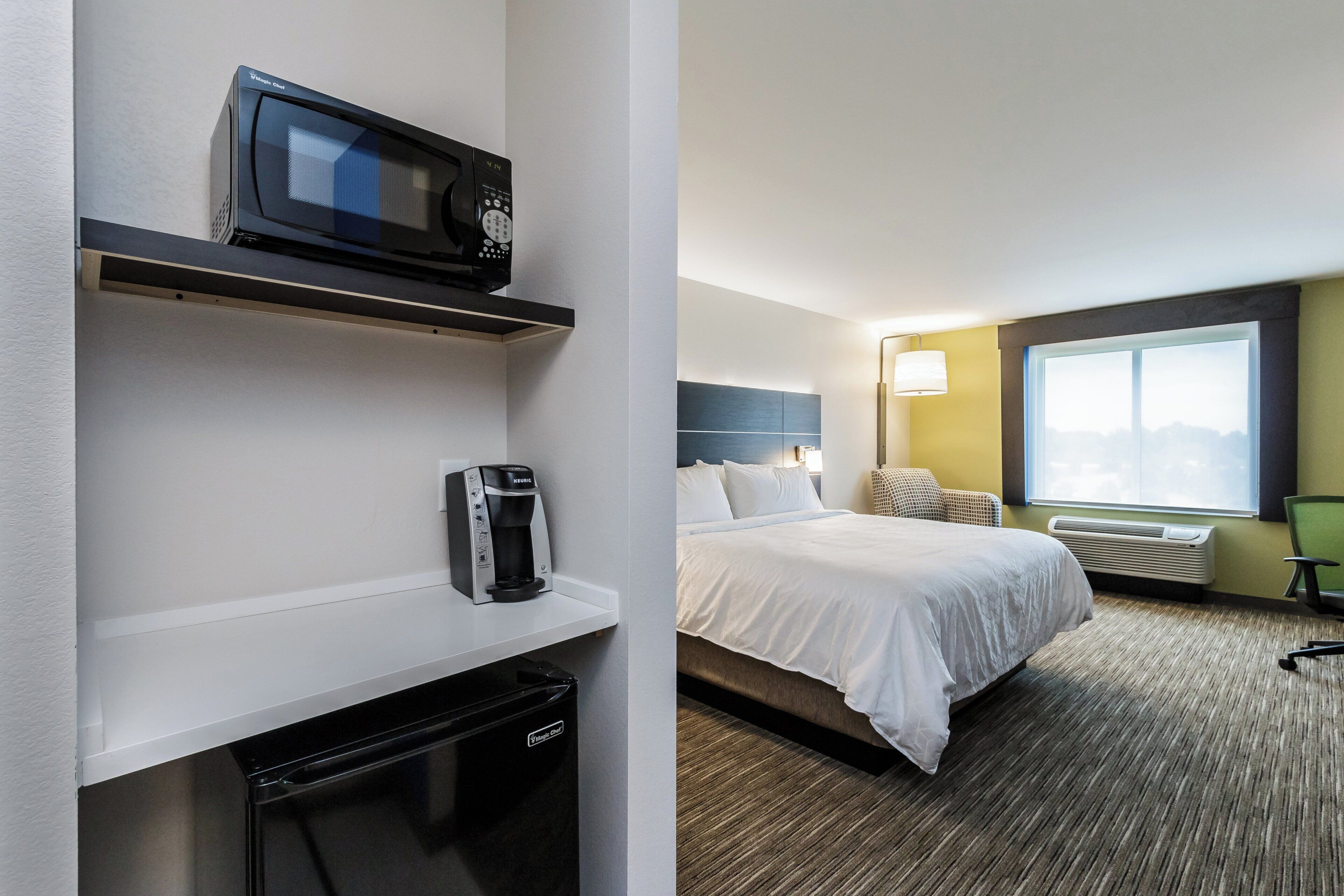 A hotel room with a bed, a microwave, a coffee maker, and a heater.