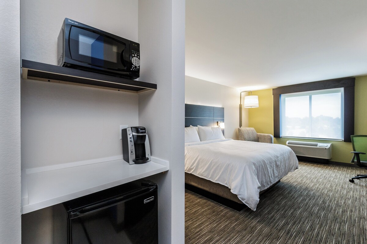 A hotel room with a bed, a microwave, a coffee maker, and a heater.