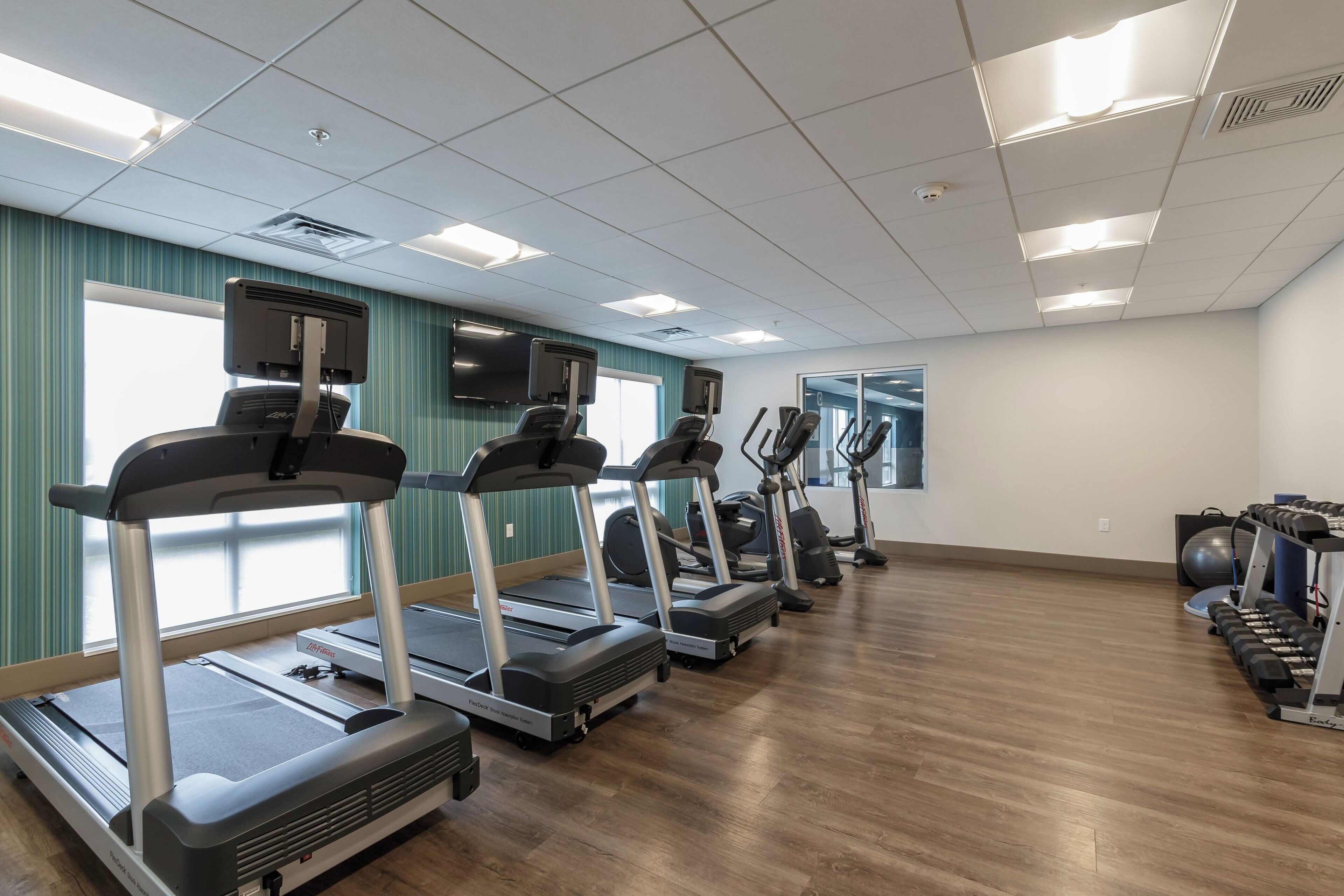 Un gimnasio con cintas de correr, pelotas de ejercicios y un espejo grande.