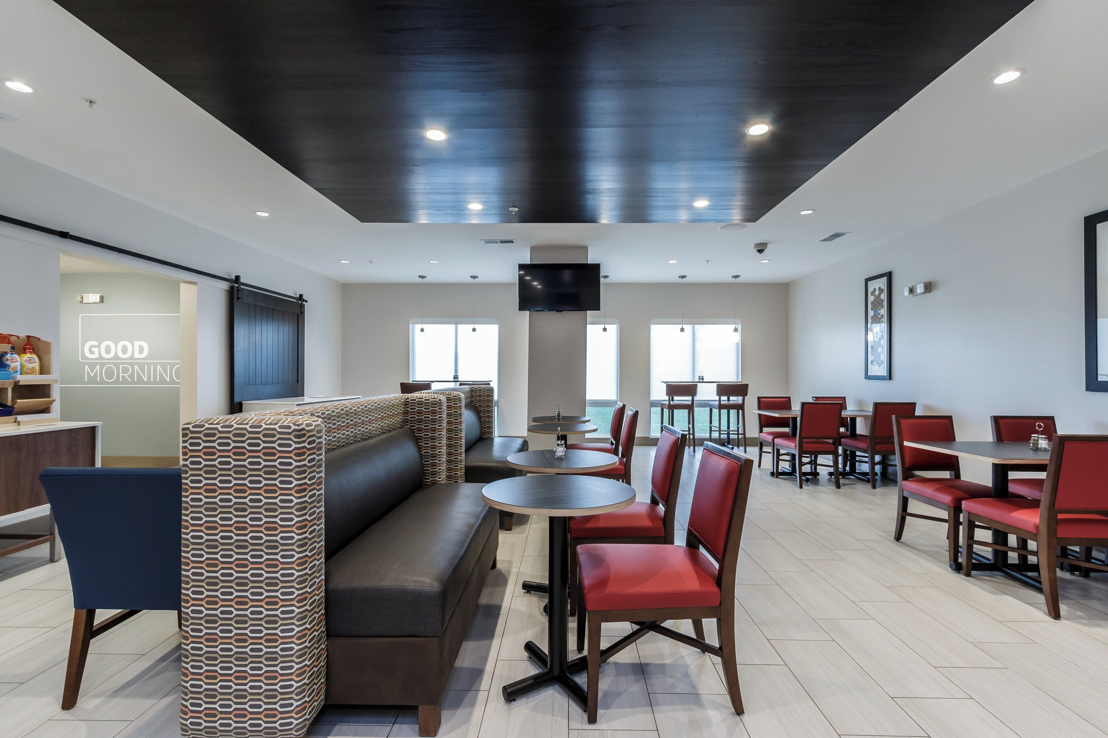 A modern restaurant interior with booths, red chairs, and a flat-screen TV mounted on the wall.