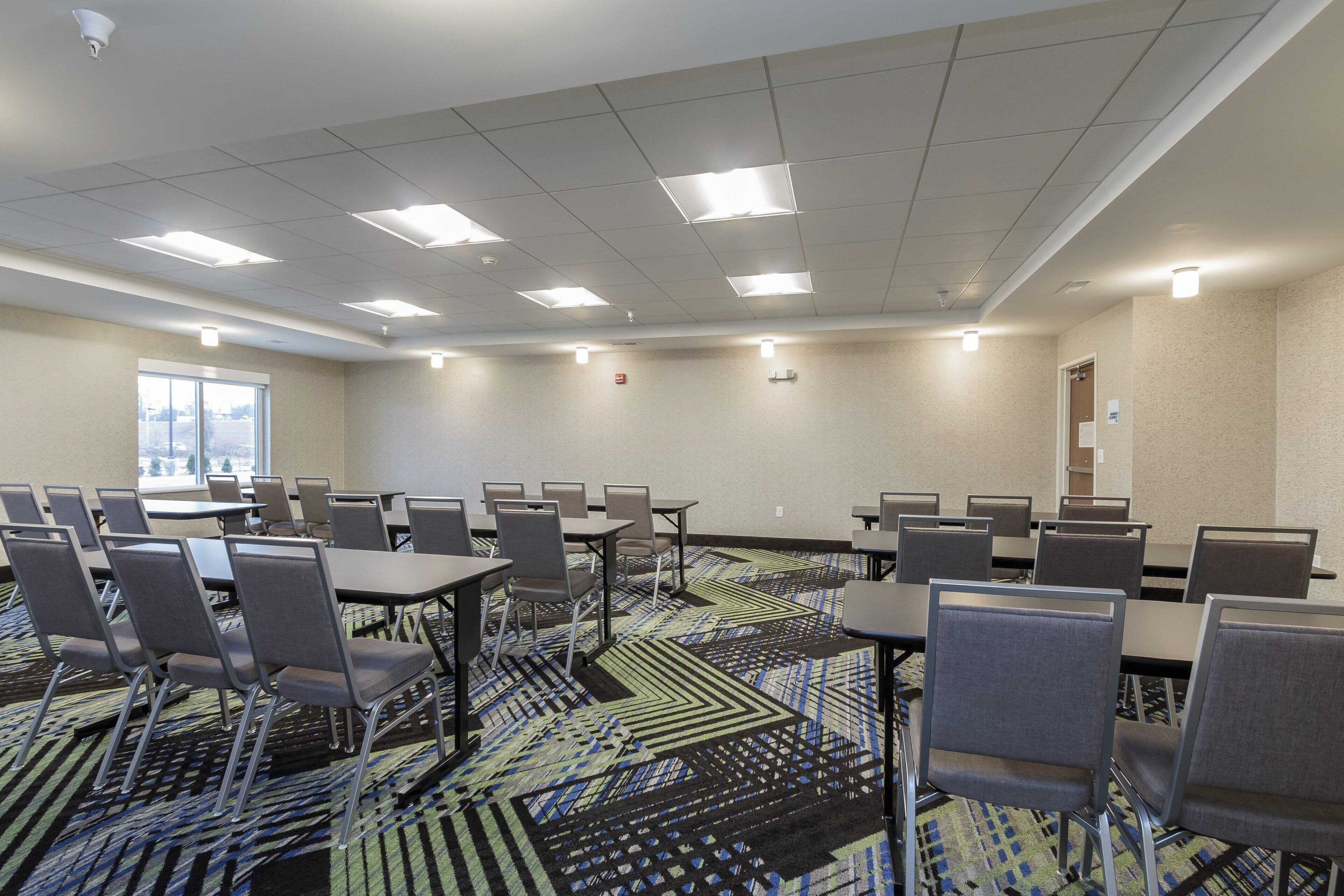 Une salle de conférence dotée de plusieurs tables et chaises, d’un tapis à motifs et d’une fenêtre offrant une vue dégagée.