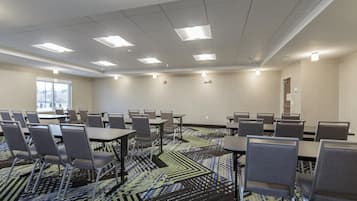 Une salle de conférence dotée de plusieurs tables et chaises, d’un tapis à motifs et d’une fenêtre offrant une vue dégagée.