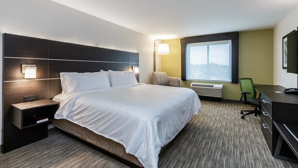A hotel room with a large bed, bedside tables, a desk, a chair, and a window with a view.