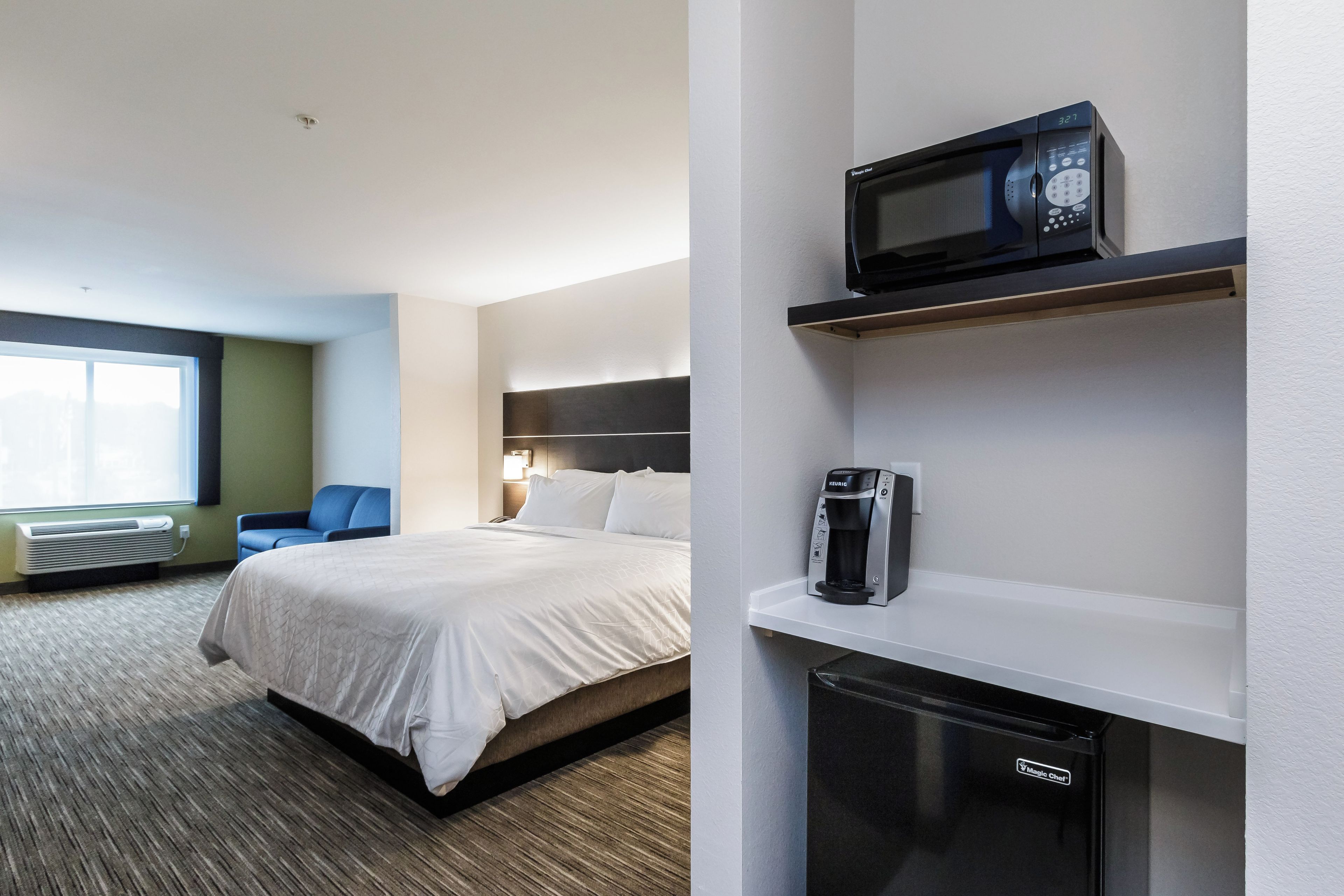 Una camera d'albergo con un letto, un forno a microonde, una macchina del caffè e un mini-frigorifero.