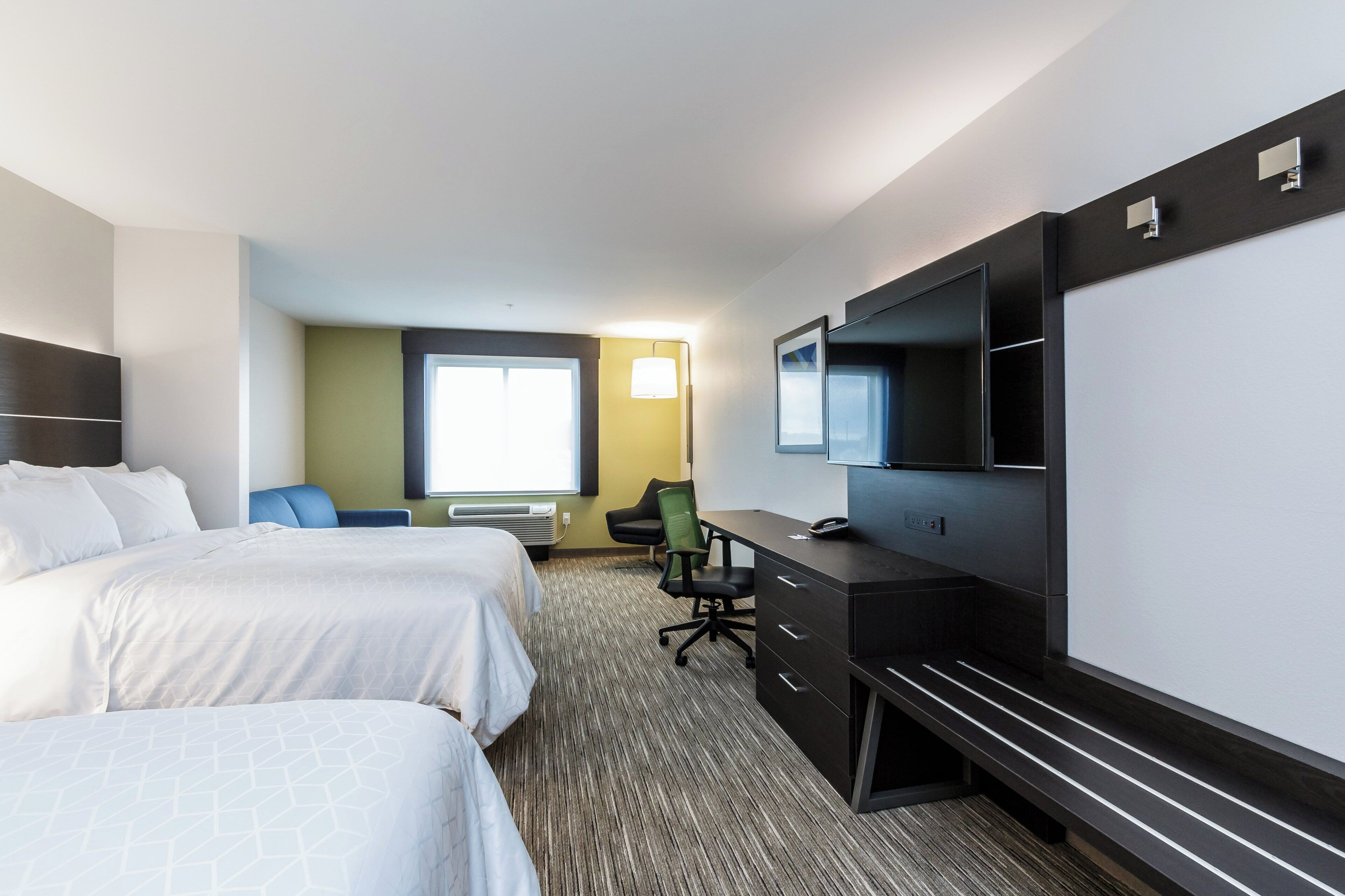 A hotel room with two beds, a desk, a chair, a television, and a window.