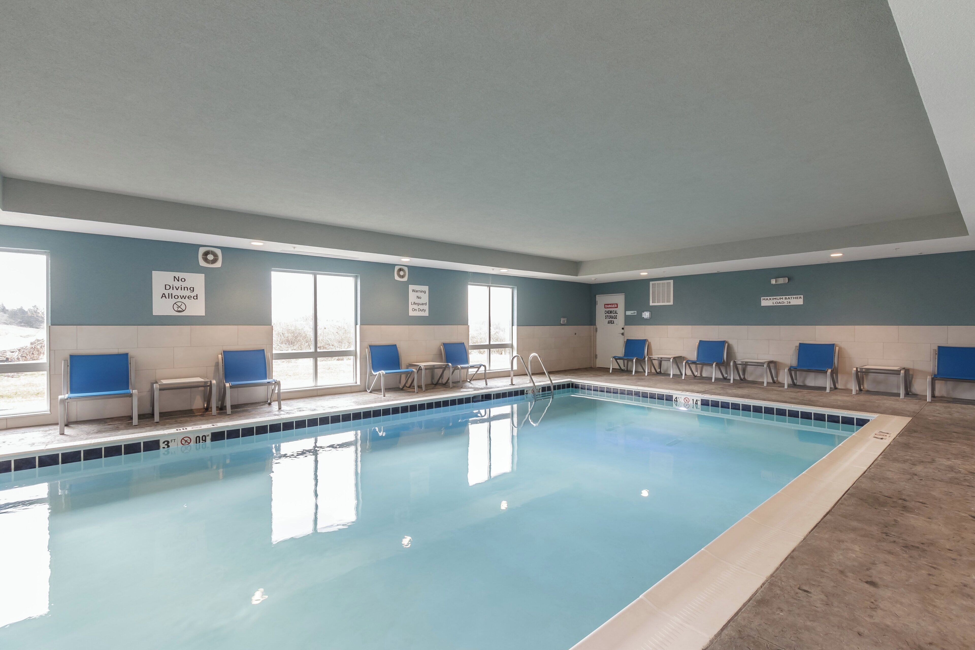 An indoor swimming pool with clear signage, including a 'No Diving Allowed' sign and a 'Maximum Bather Load' sign.
