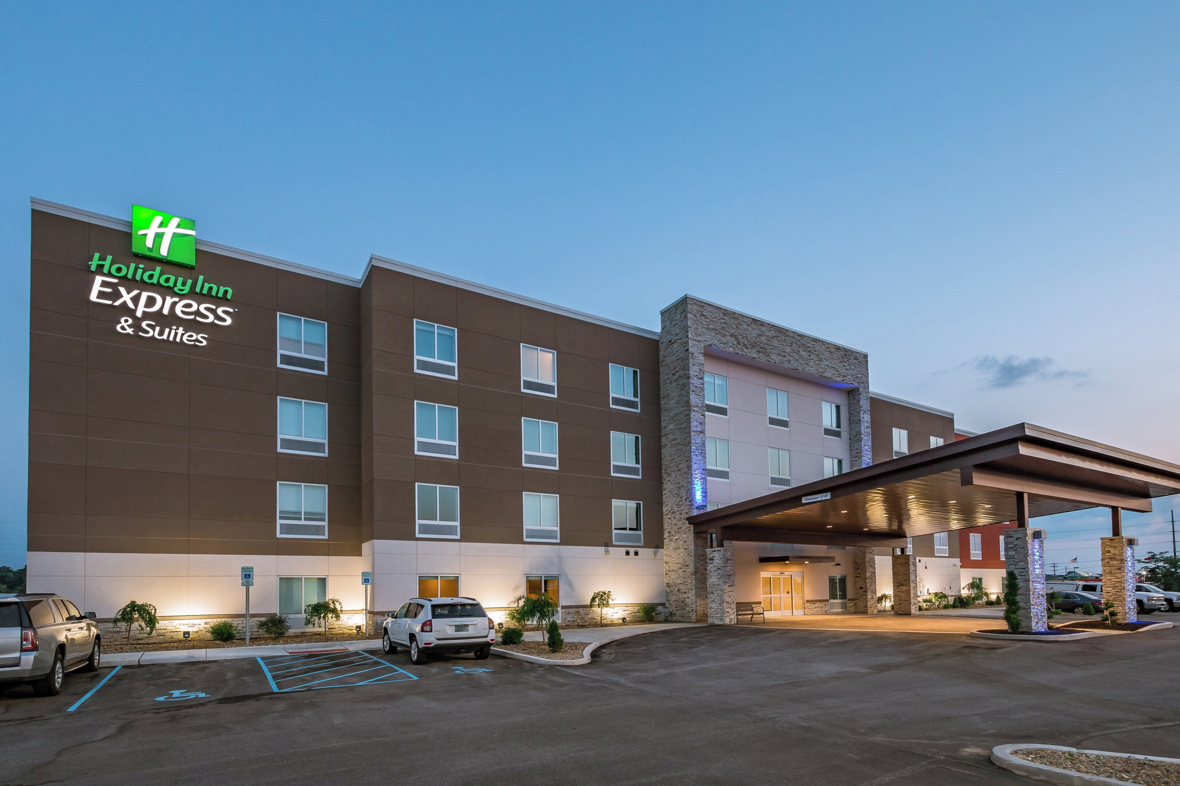 Un edificio de Holiday Inn Express & Suites con un diseño moderno, que presenta un techo plano, varias ventanas y un área de entrada cubierta.