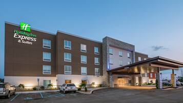 Un edificio de Holiday Inn Express & Suites con un diseño moderno, que presenta un techo plano, varias ventanas y un área de entrada cubierta.