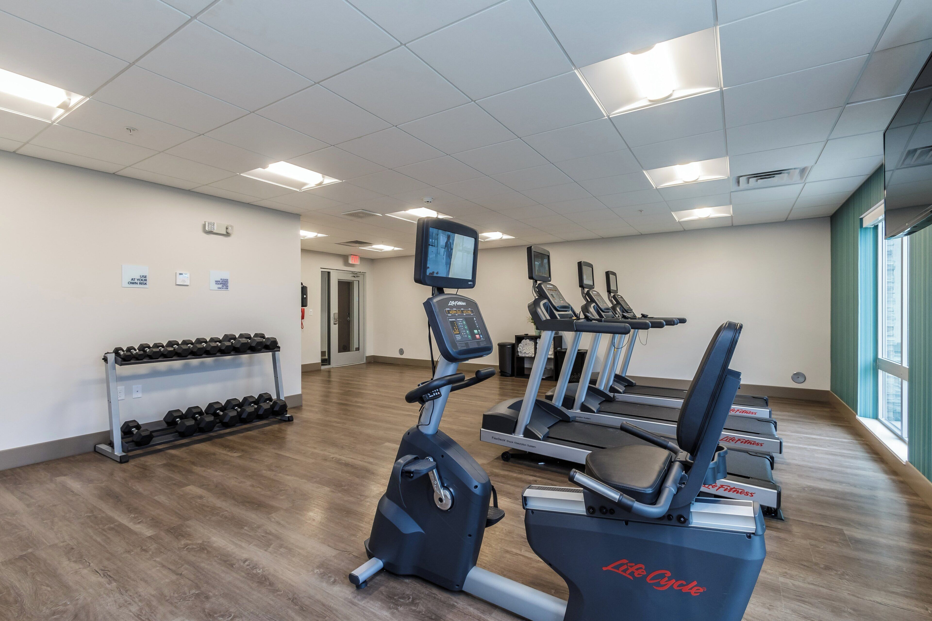 A gym with treadmills, elliptical machines, and a rack of dumbbells.