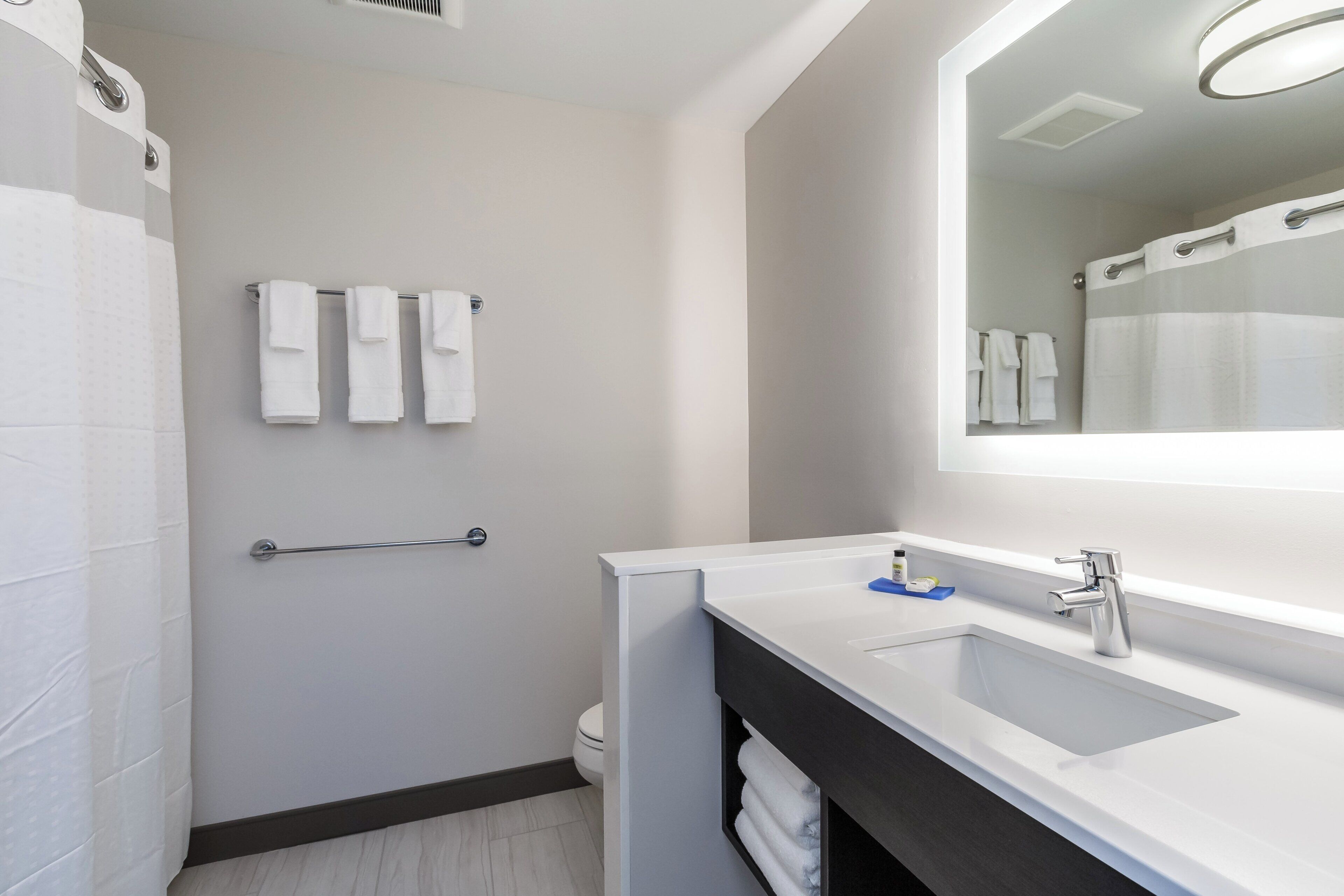 A modern bathroom with a white sink, a large mirror, and a towel rack with three towels.