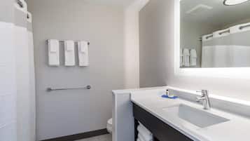 A modern bathroom with a white sink, a large mirror, and a towel rack with three towels.