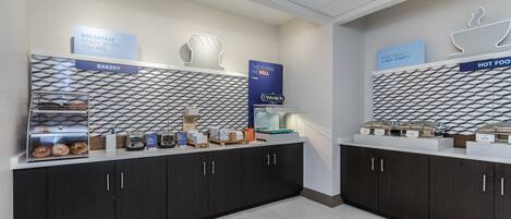 A breakfast area with a bakery and hot food station, featuring a geometric patterned backsplash and modern cabinetry.