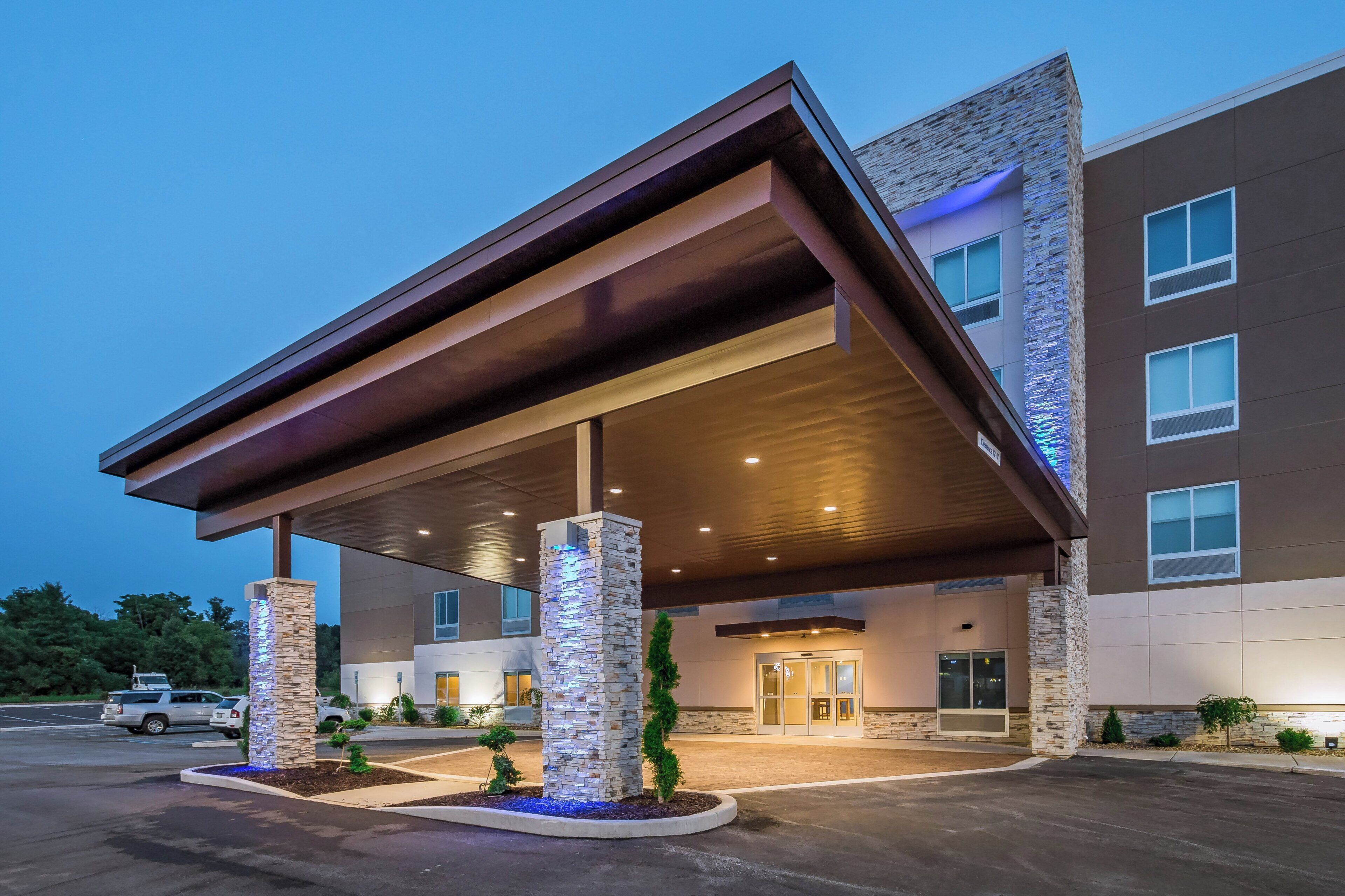 L’entrée d’un hôtel, avec une allée couverte, des piliers en pierre et une façade de bâtiment moderne.