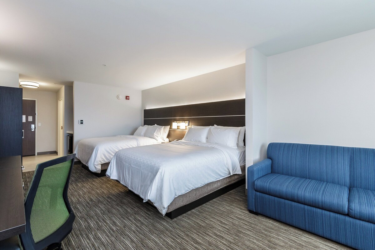 A hotel room with two beds, a sofa, a desk, and a chair.