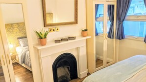 Un dormitorio con chimenea, cama, espejo y ventana con cortinas.
