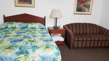 Un dormitorio con una cama, una mesita de noche, una lámpara, un sillón a rayas y dos cuadros en la pared.