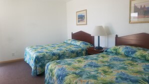 Une chambre avec deux lits simples, chacun agrémenté d’une couvre-lit à motifs floraux, d’une tête de lit en bois, d’une table de chevet avec une lampe et d’un tableau encadré au mur.