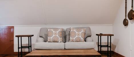 Ein Wohnzimmer mit grauem Sofa, zwei gemusterten Zierkissen, einem Holztisch und zwei schwarzen Beistelltischen.