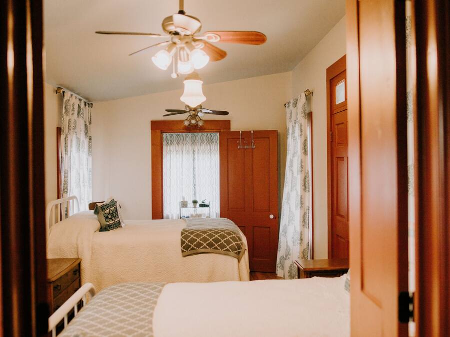 A bedroom with two beds, a ceiling fan, and a wooden door.