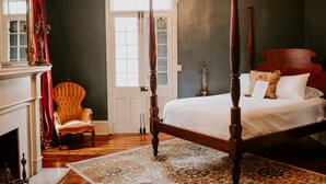 A four-poster bed with a white bedspread, a wooden chair, a fireplace, and a chandelier. - Mouton Plantation (Lafayette)