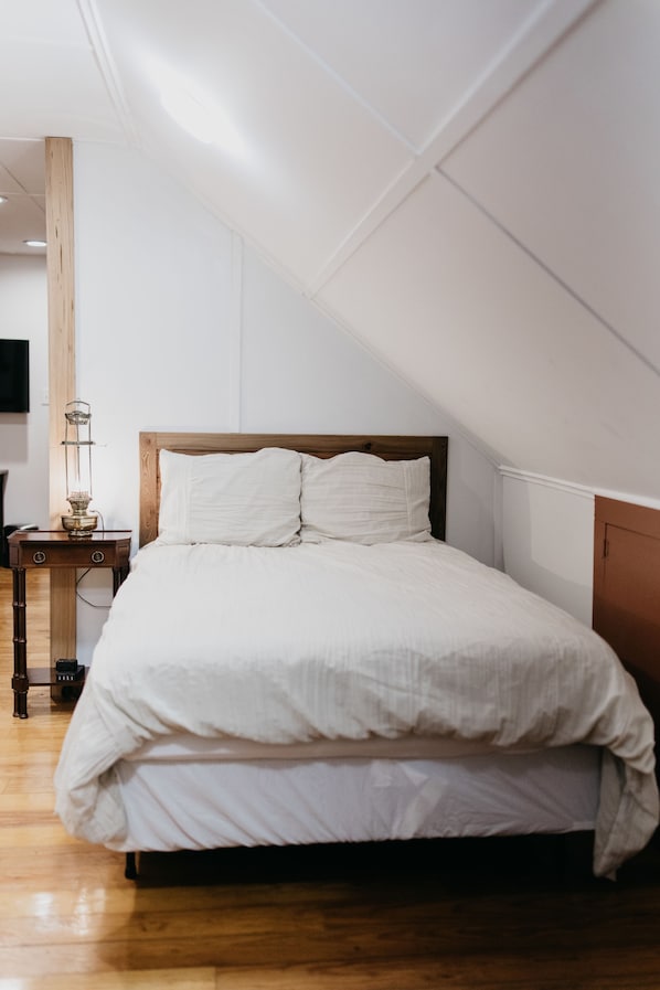Une chambre à coucher avec une tête de lit en bois, un couvre-lit blanc et une table de chevet avec une lampe.