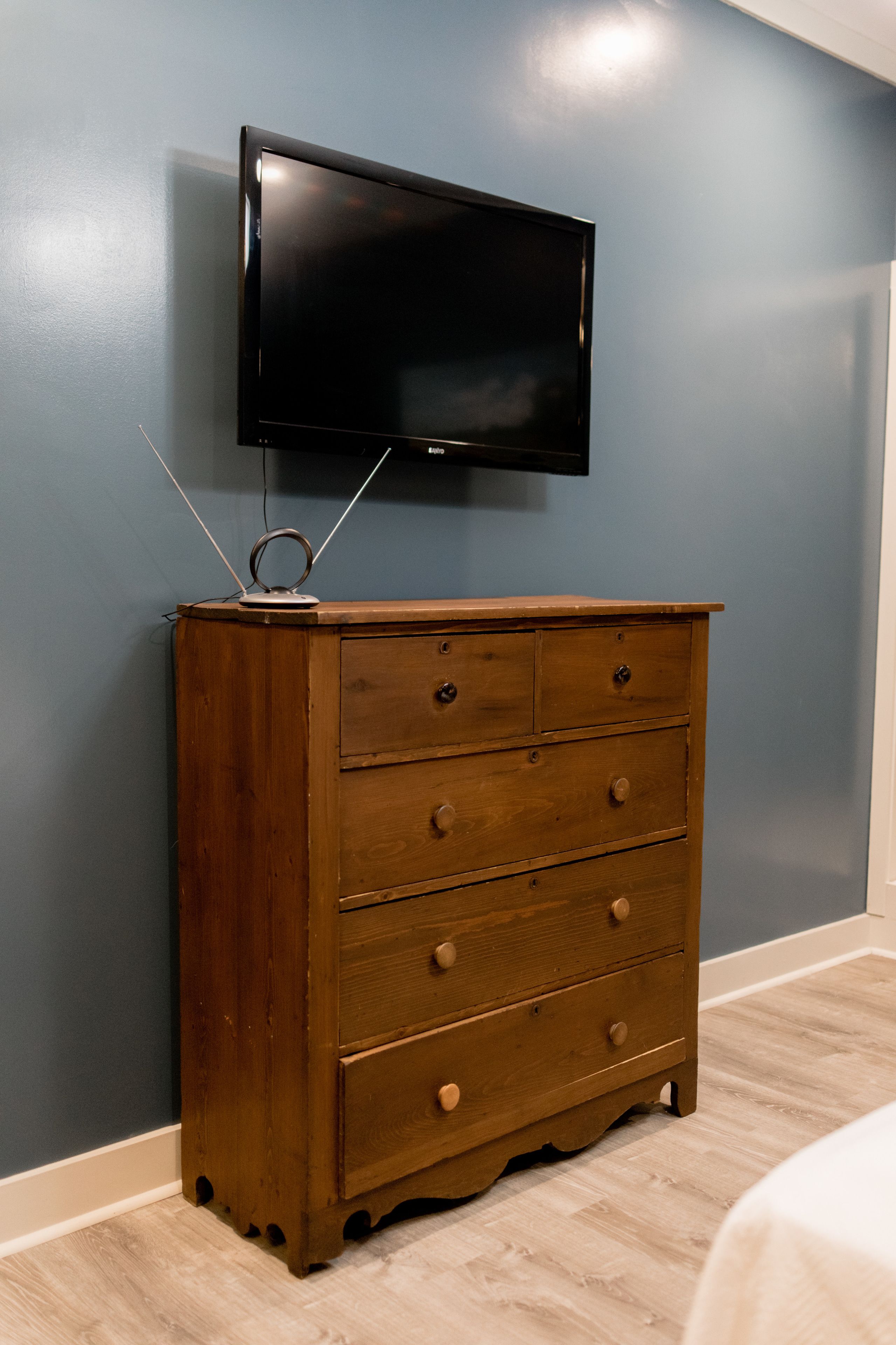 A wooden dresser with drawers and a flat-screen TV mounted above it.