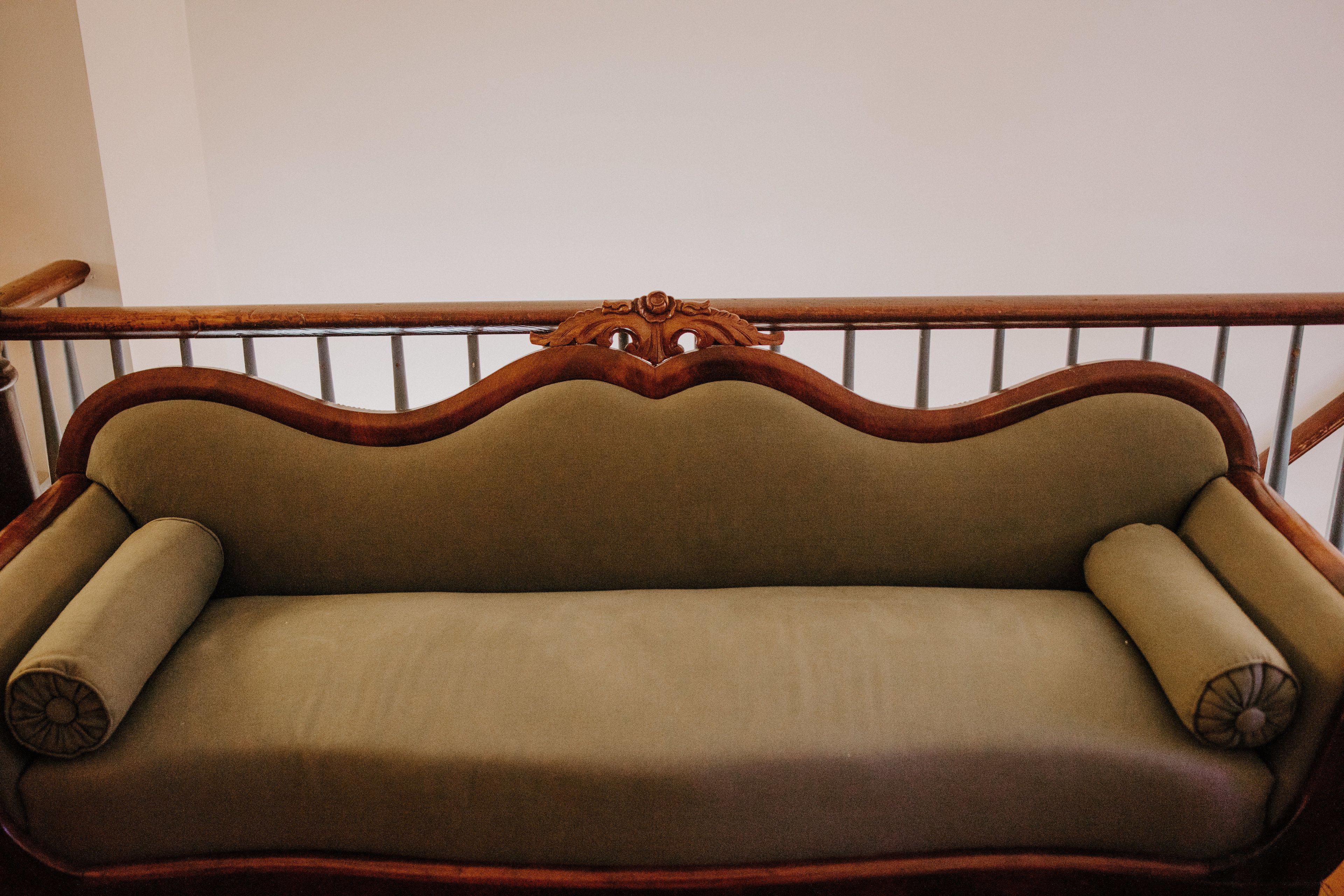 A wooden bench with a curved backrest and armrests, upholstered in a light fabric.