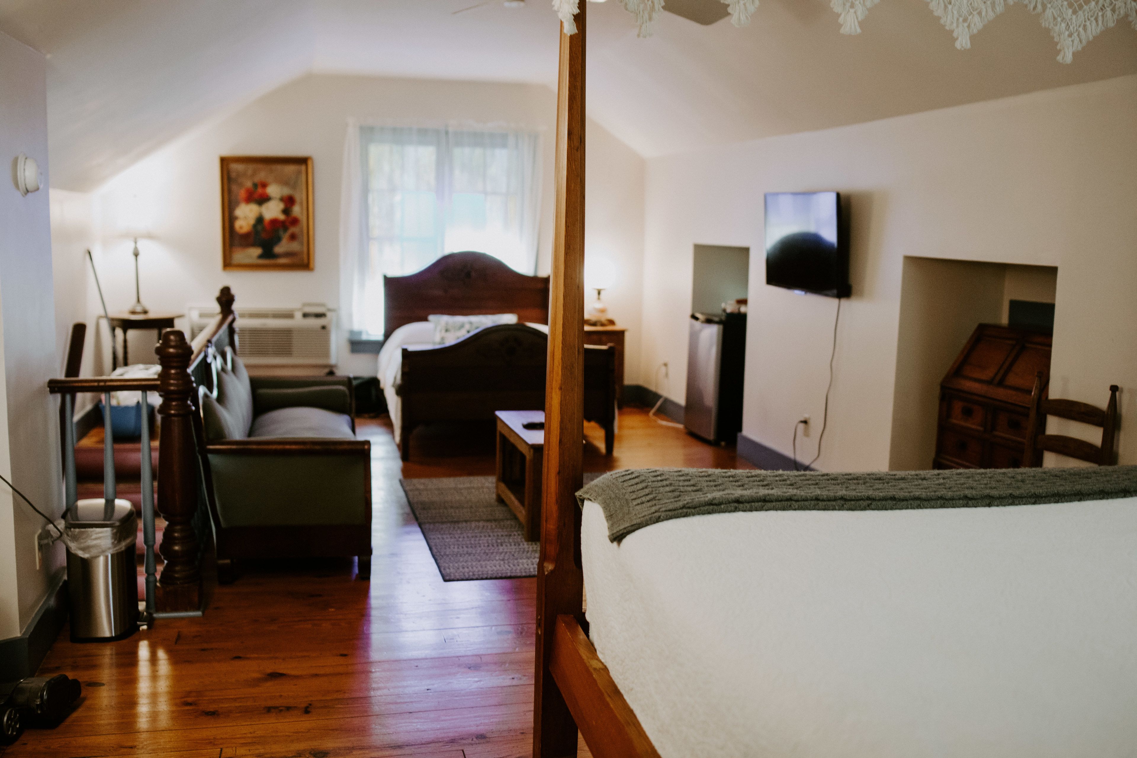 Een slaapkamer met een hemelbed, een houten dressoir, een televisie en een schilderij aan de muur.