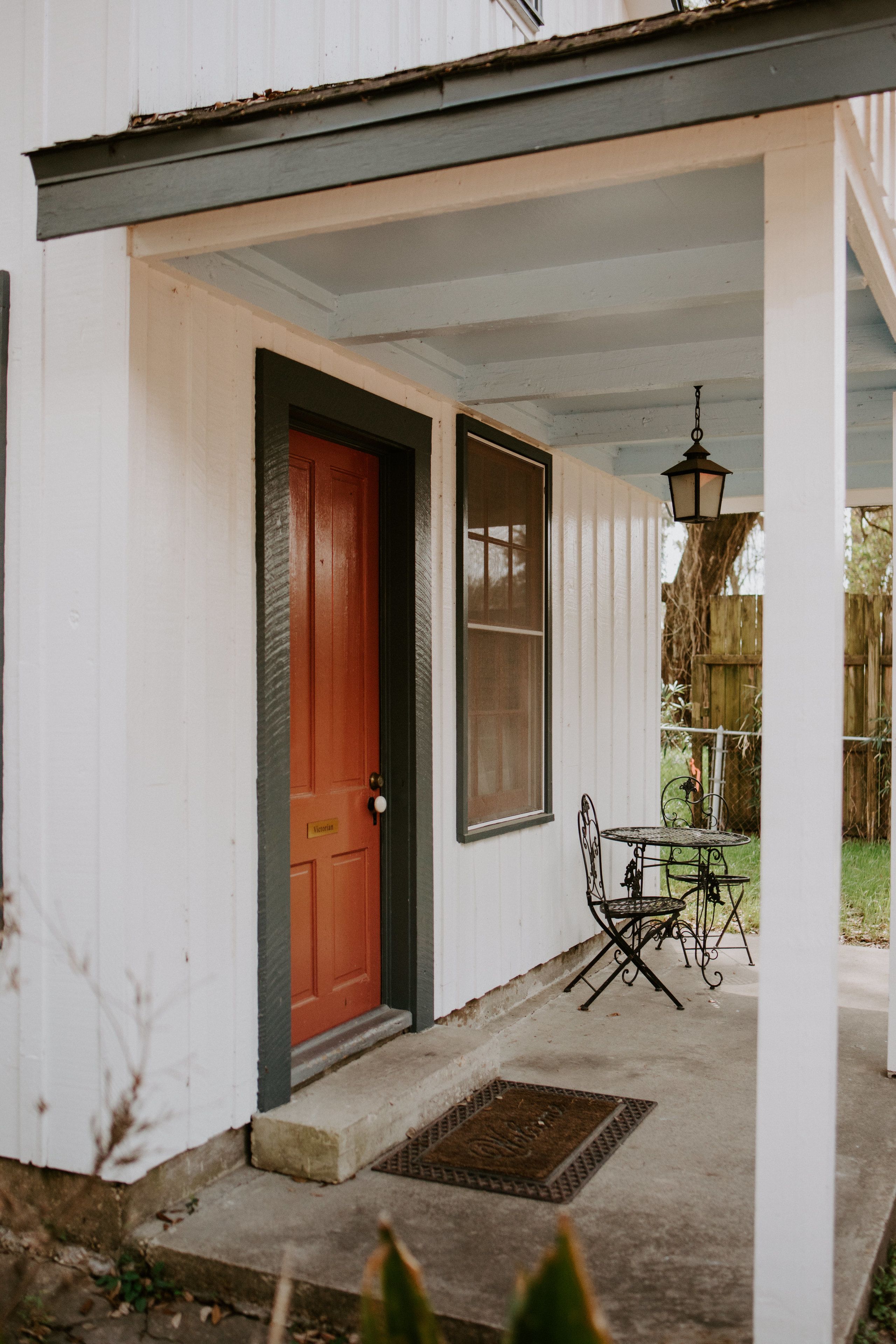 A white building with a red door, a window, and a small outdoor table with chairs.