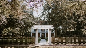 A gated entrance to a building with a white facade and a covered walkway leading to the entrance. - Mouton Plantation (Lafayette)
