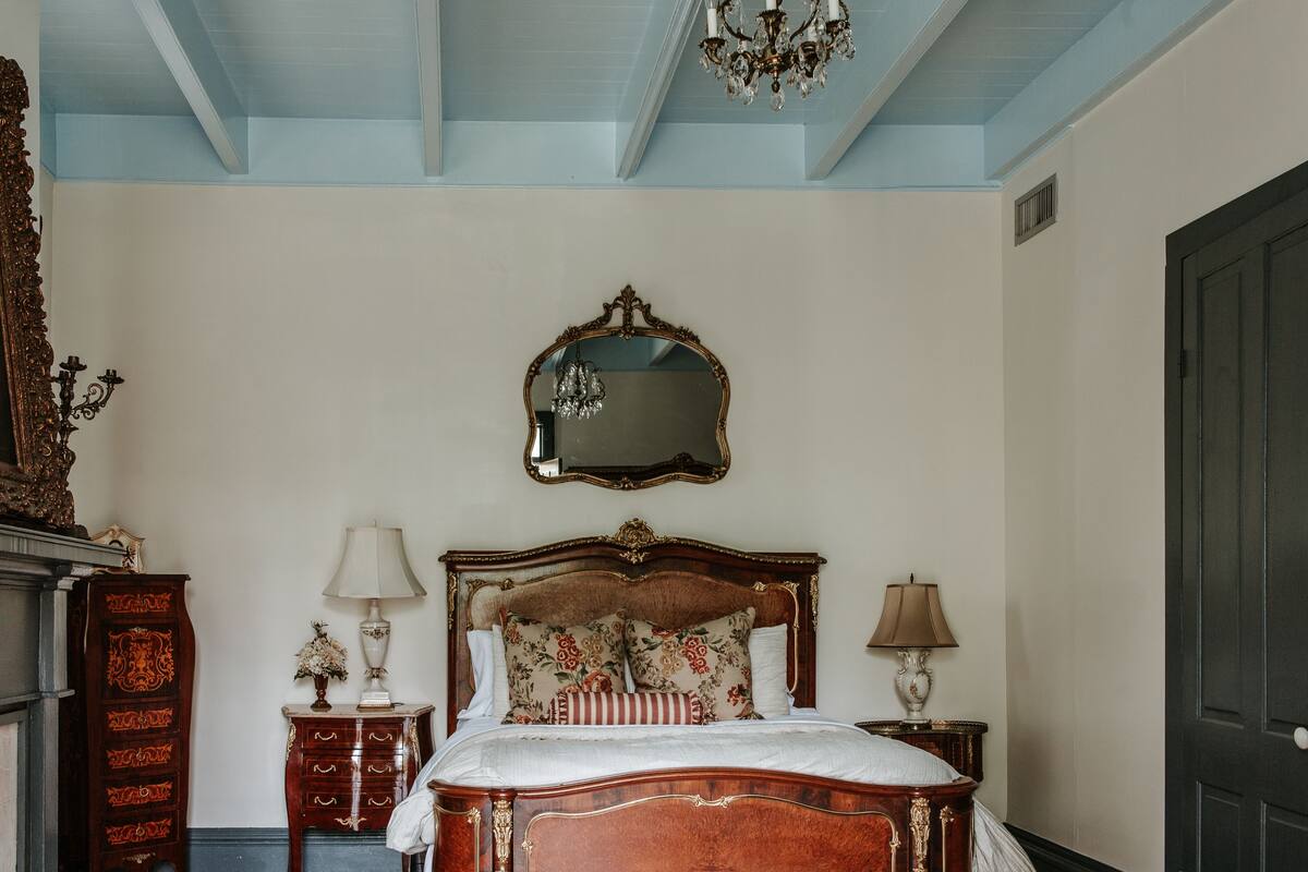 Une chambre à coucher avec un grand lit, une tête de lit décorée, un miroir et un lustre.