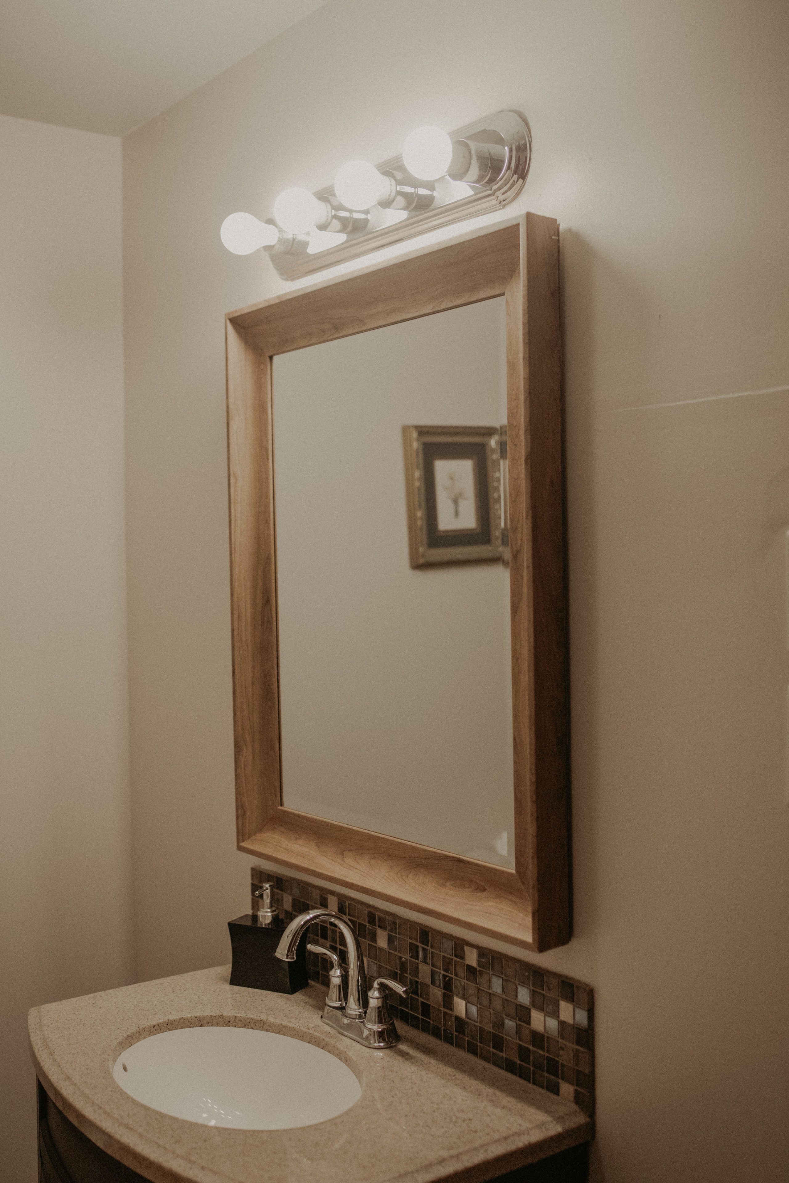 Ein Badezimmer mit einem spiegelnden Holzbruch, einem Waschbecken mit Wasserhahn und einer gefliesten Rückwand.