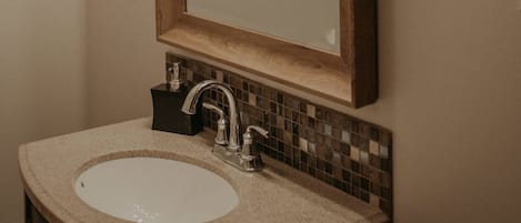 Ein Badezimmer mit einem spiegelnden Holzbruch, einem Waschbecken mit Wasserhahn und einer gefliesten Rückwand.