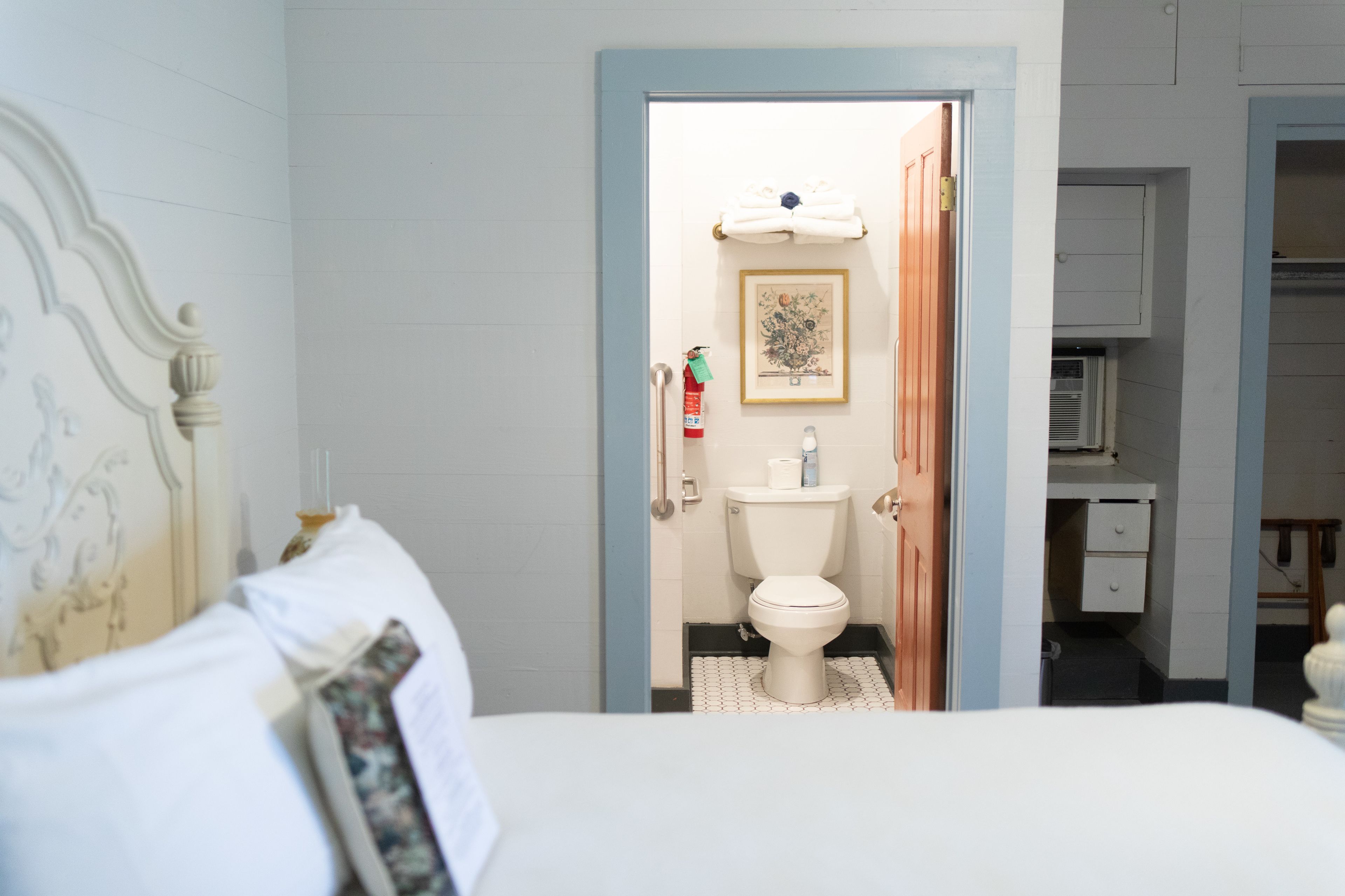 A bedroom with a bed, a bathroom visible through an open door, and a small desk area.