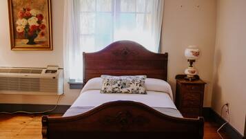 A bedroom with a wooden bed, a bedside table with a lamp, a radiator, and a window with curtains.