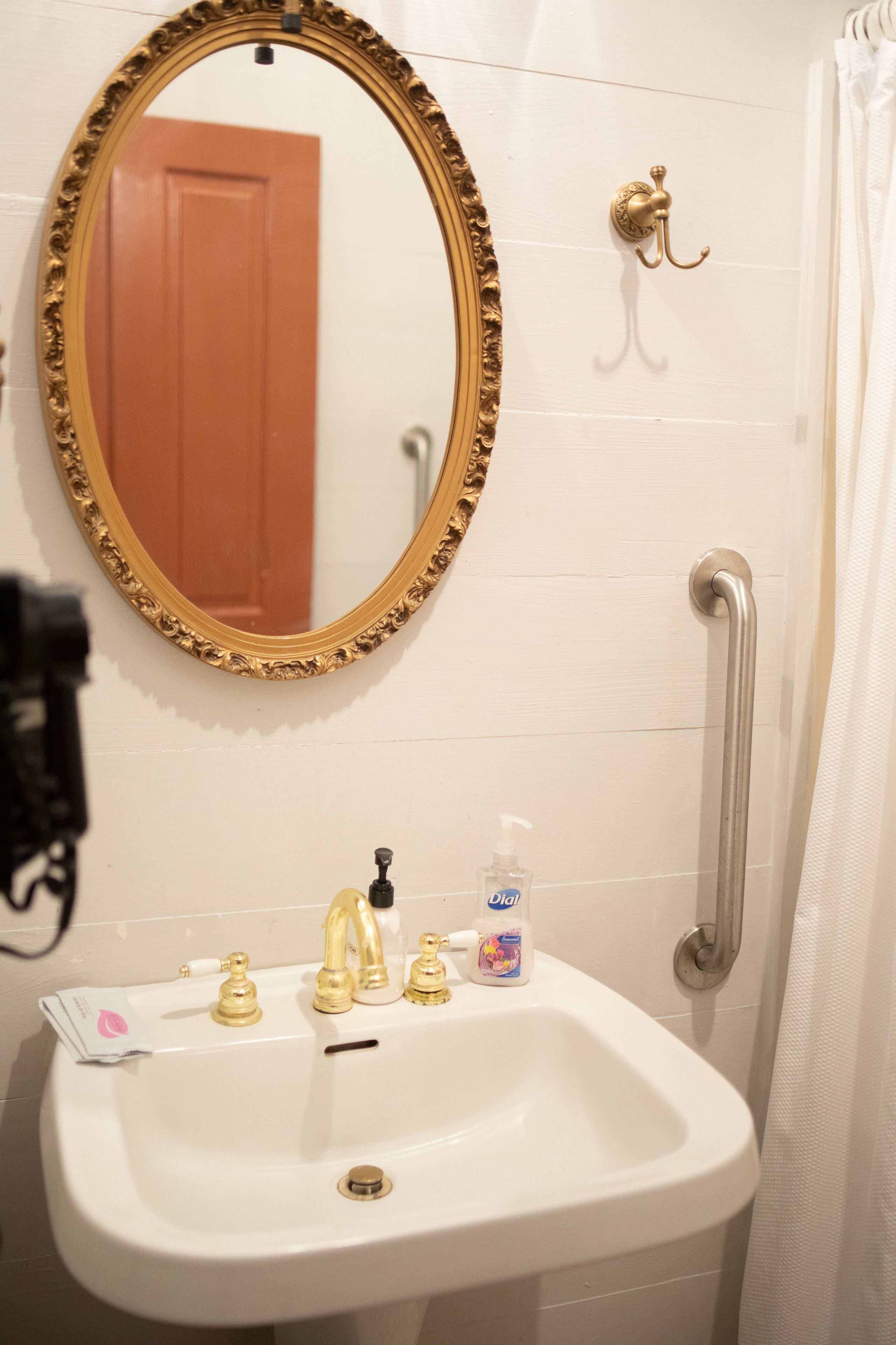 A bathroom with a white sink, gold faucets, a gold-framed mirror, a door, and a grab bar.
