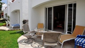 Eine Terrasse mit Gartenmöbeln, einem Glastisch und einer Glasschiebetür, die zu einem Innenbereich führt.