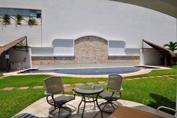 A pool area with a stone wall, two chairs, and a table.
