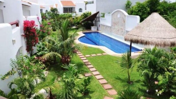 Ein Pool, umgeben von üppiger Vegetation und weißen Gebäuden mit roten Akzenten.