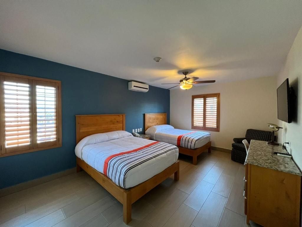 Un dormitorio con dos camas de madera, un ventilador de techo, un equipo de aire acondicionado, un televisor y una pequeña zona de escritorio.