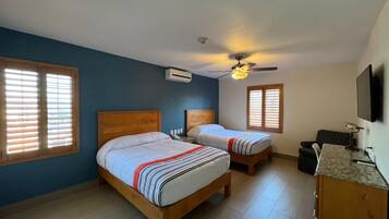 Un dormitorio con dos camas de madera, un ventilador de techo, un equipo de aire acondicionado, un televisor y una pequeña zona de escritorio.