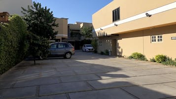 Uma área de estacionamento com dois carros, um edifício de fachada bege e uma árvore.