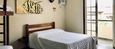 A bedroom with a wooden bed, a painting of fish, an air conditioner, and a view of the outside.
