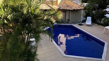 A swimming pool with a tiled edge, surrounded by palm trees and a building with a tiled roof.