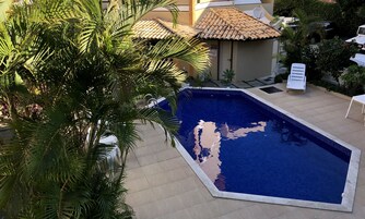 Una piscina con borde de azulejos, rodeada de palmeras y un edificio con techo de tejas.