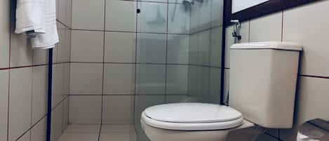 Un baño con inodoro, cabina de ducha de vidrio y toalla colgada en la pared.